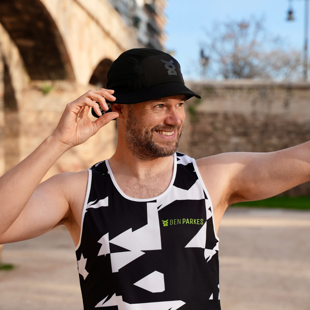 Man wearing a black and white geometric running singlet top with 'Ben Parkes' branding outdoors. He's also wearing a black bucket running hat