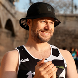 Man wearing a black running bucket hat and a sleeveless shirt with a logo, standing outdoors.